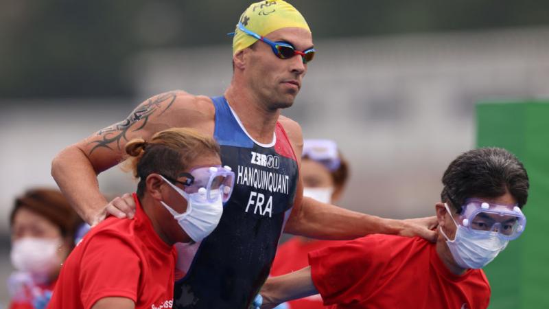 A male triathlete is assisted by staff after the swim segment at the Tokyo 2020 Paralympics