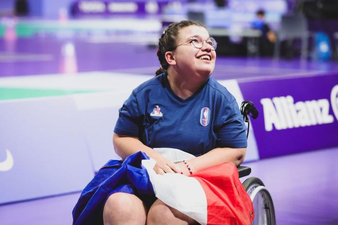 Aurelie Aubert, a French boccia athlete, smiles and holds a French flag to celebrate her victory at the Paris 2024 Paralympics