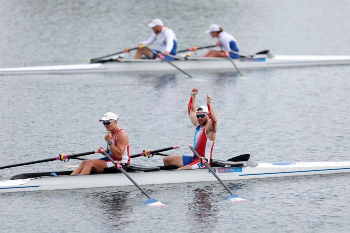 Two athletes, one male and one female, on a rowing boat are pumping their fist in celebration