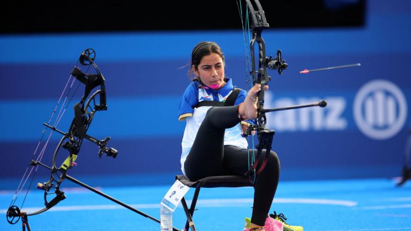 A woman shoots an arrow, holding the bow with her foot