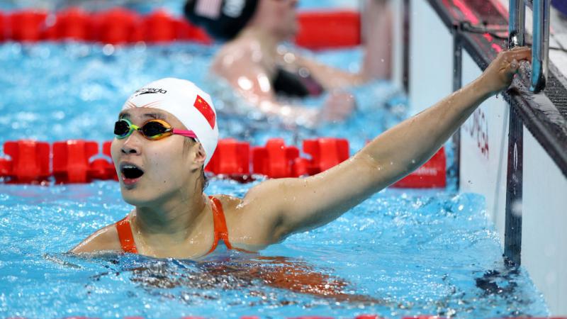 woman in goggles and speedo cap holds on to the edge of the pool and looks up shocked