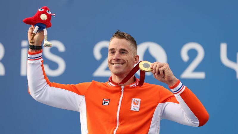 Para cyclist Jetze Plat holding up a gold medal and smiling 