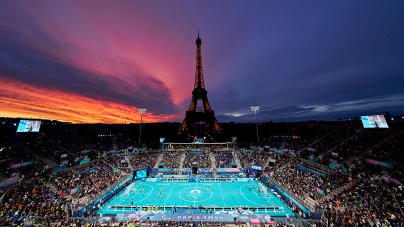 A view of the outdoor Paris 2024 blind football stadium at sunset, with the Eiffel Tower in the background
