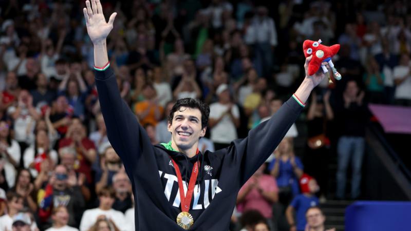 A man in a Team Italy sweater wearing a gold medal raises his arms in the air in celebration in front of a crowd of people at La Defense Arena
