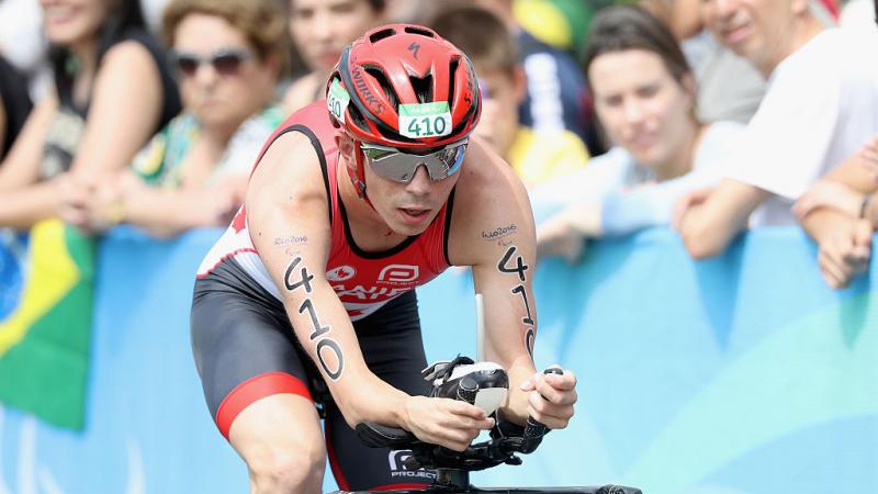 Stefan Daniel in a red Canada kit leans forward on his bike in front of a crowd at Rio 2016
