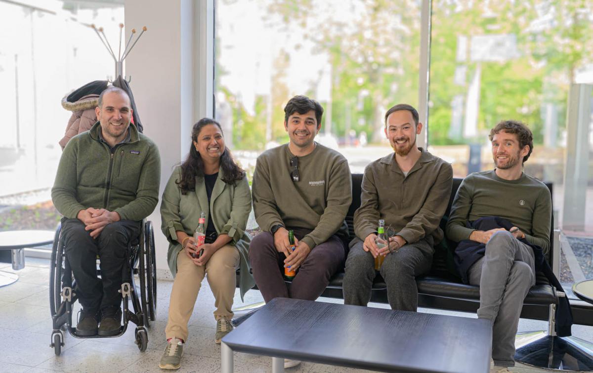 Five IPC staff members smile for a photo in front of a glass window