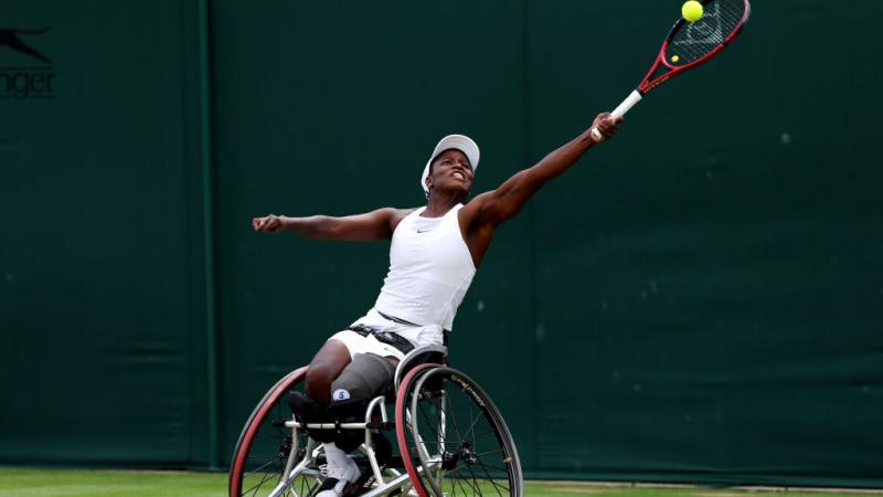 A female wheelchair tennis player stretches to play a forehand during a match.