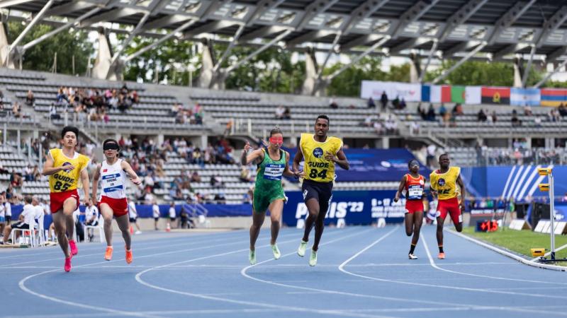 Three female runners with male guides in a Para athletics race